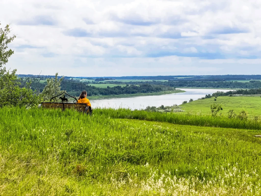 Saskatoon Day Trips Person sitting on a bench looking at the view of the South Saskatchean River from a walking trail at Batoche National Historic Site