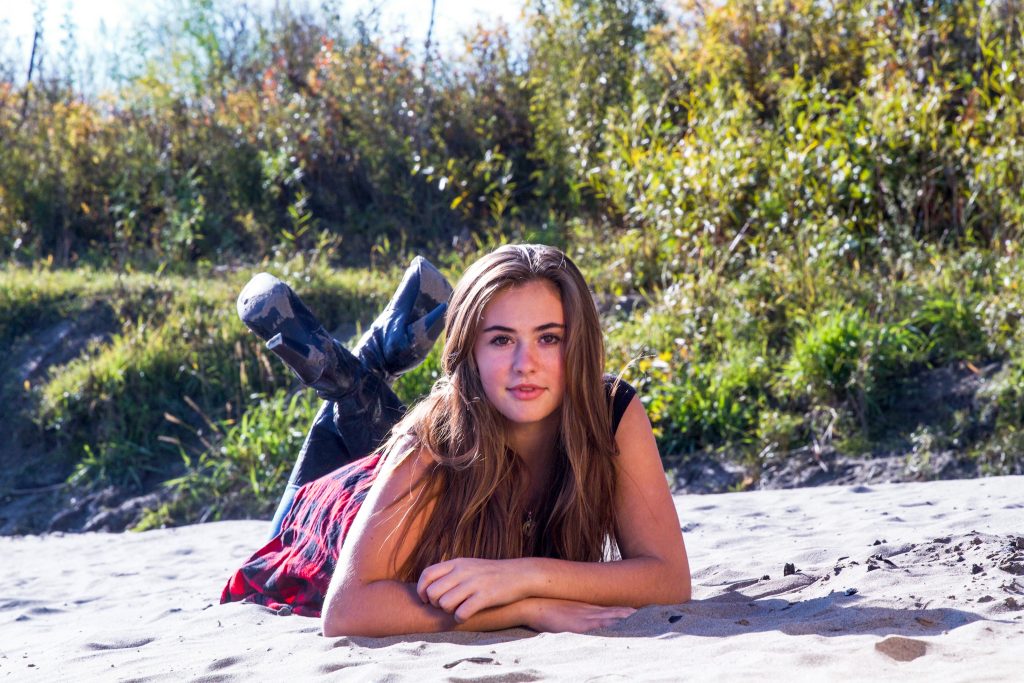 Teenage girl posing for photos on the sandy shoreline near Borden Bridge along North Saskatchewan River.