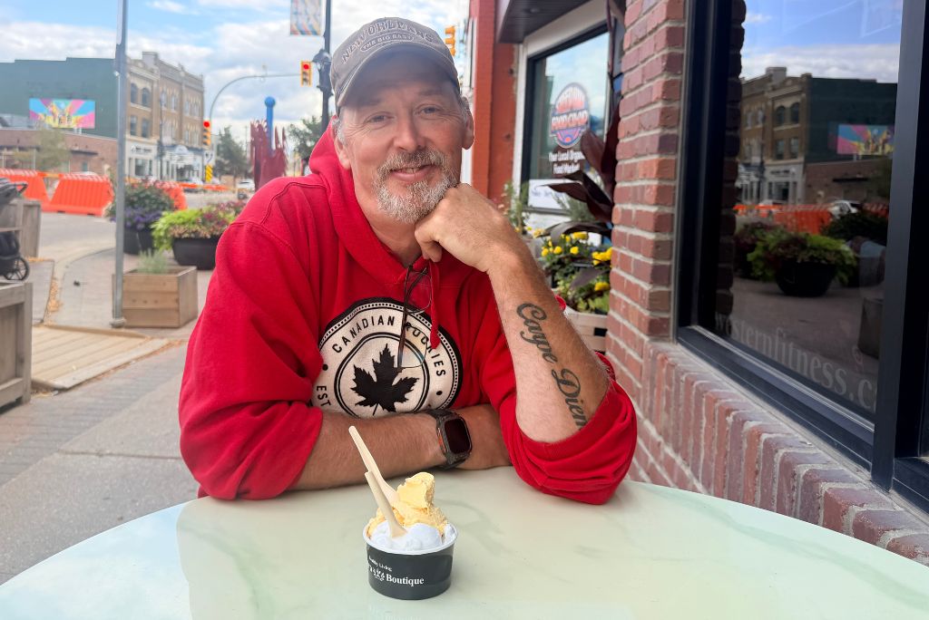 Man sitting outside posing in front of a patio table on Broadway Avenue with gelato in a bowl.