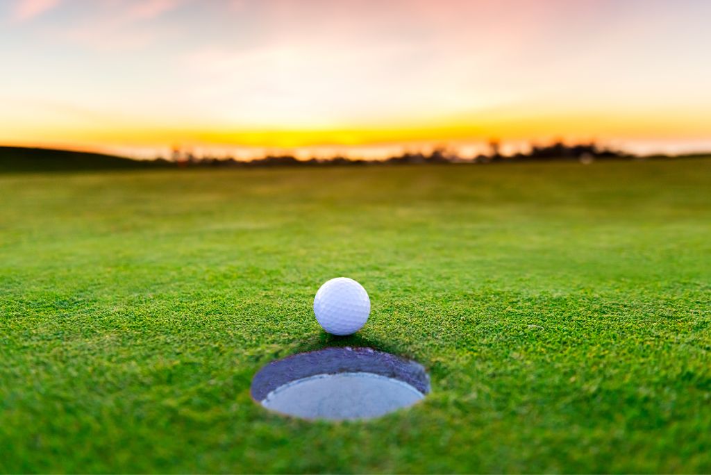 Best Activities in Saskatoon Golf ball sitting beside a hole on a putting green with a sunset in the background.
