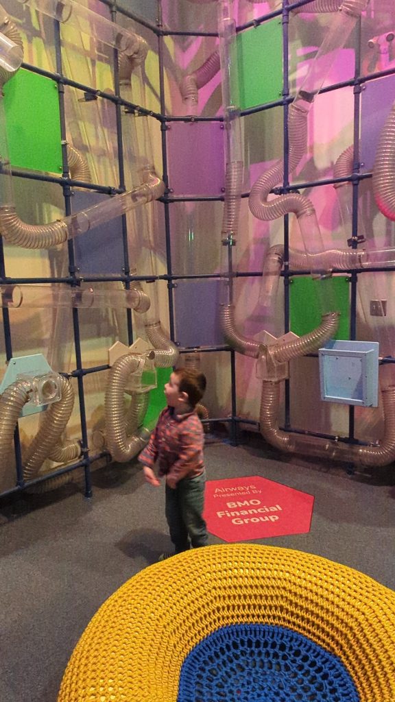 Child playing with interactive air tube exhibit at Nutrien Wonderhub children’s museum in Saskatoon, featuring colorful walls and hands-on learning displays