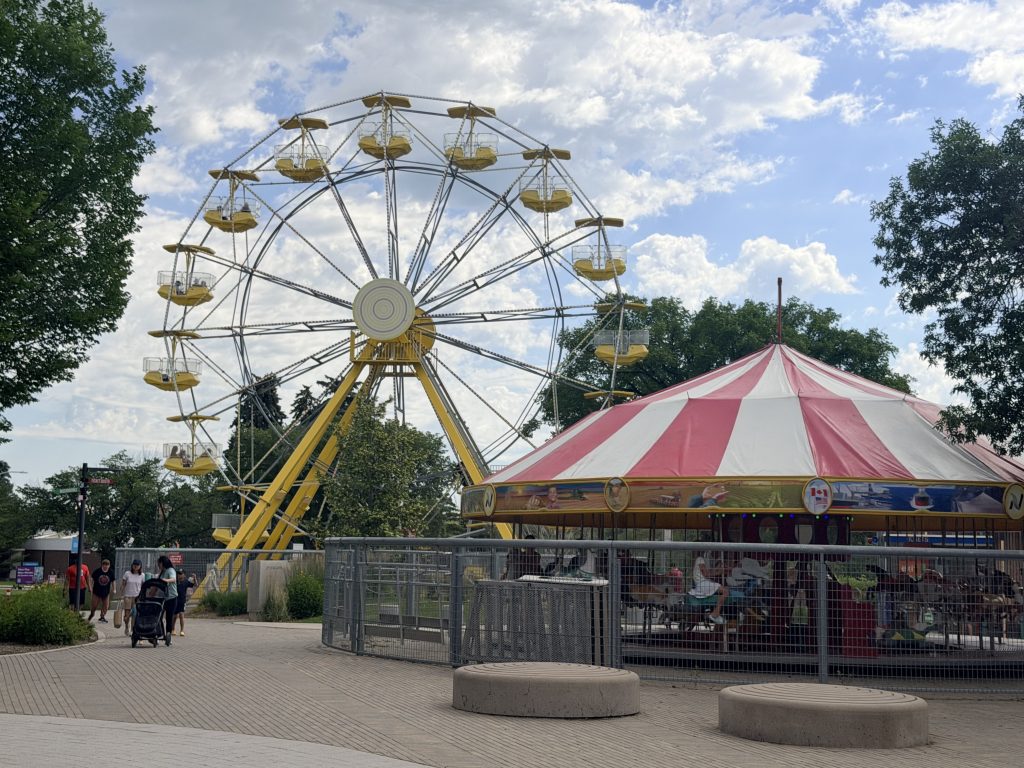 Best Activities in Saskatoon Ferris wheel and carousel at Kinsmen Park in Saskatoon on a sunny summer day with blue skies and families enjoying the amusement rides.
