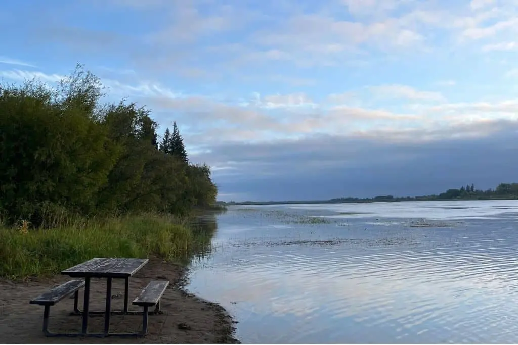 Picnic table beside the shoreline at Pike Lake Provincial Park with calm water and trees along the shore.
