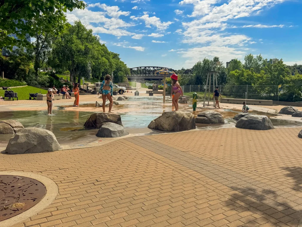 Best activities in Saskatoon Children playing at the River Landing Spray park under sunny skies in downtown Saskatoon