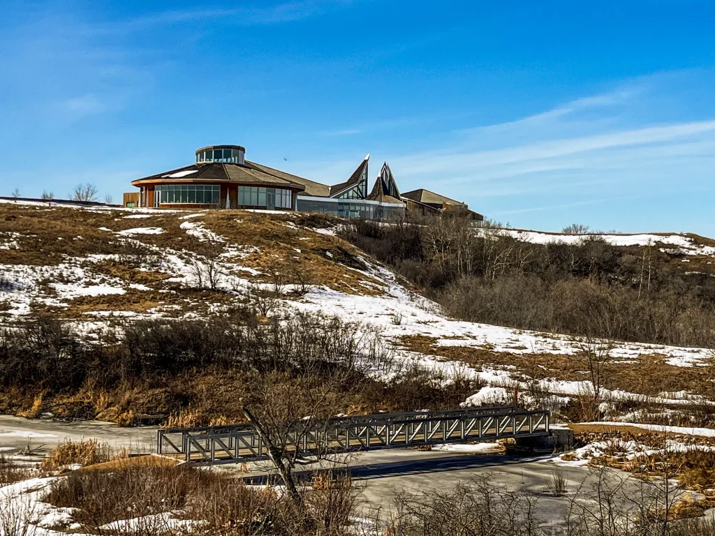 Wanuskewin Heritage Park in early spring with snow patches, walking trails, and the interpretive centre overlooking the prairie valley in Saskatoon
