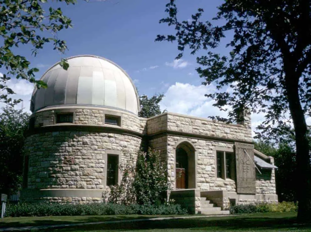 Historic University of Saskatchewan observatory surrounded by trees on a clear day.