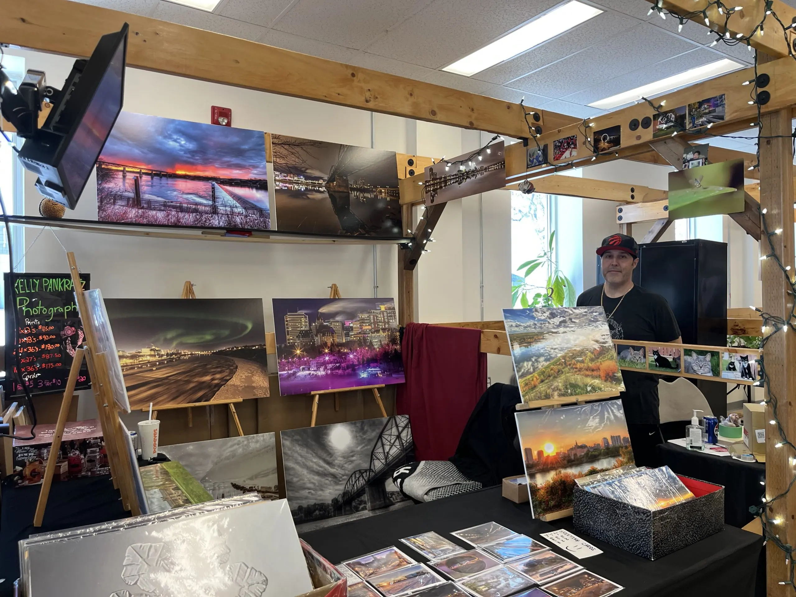Local photographer selling landscape prints and cards at a vendor booth inside a Saskatoon farmer’s market.