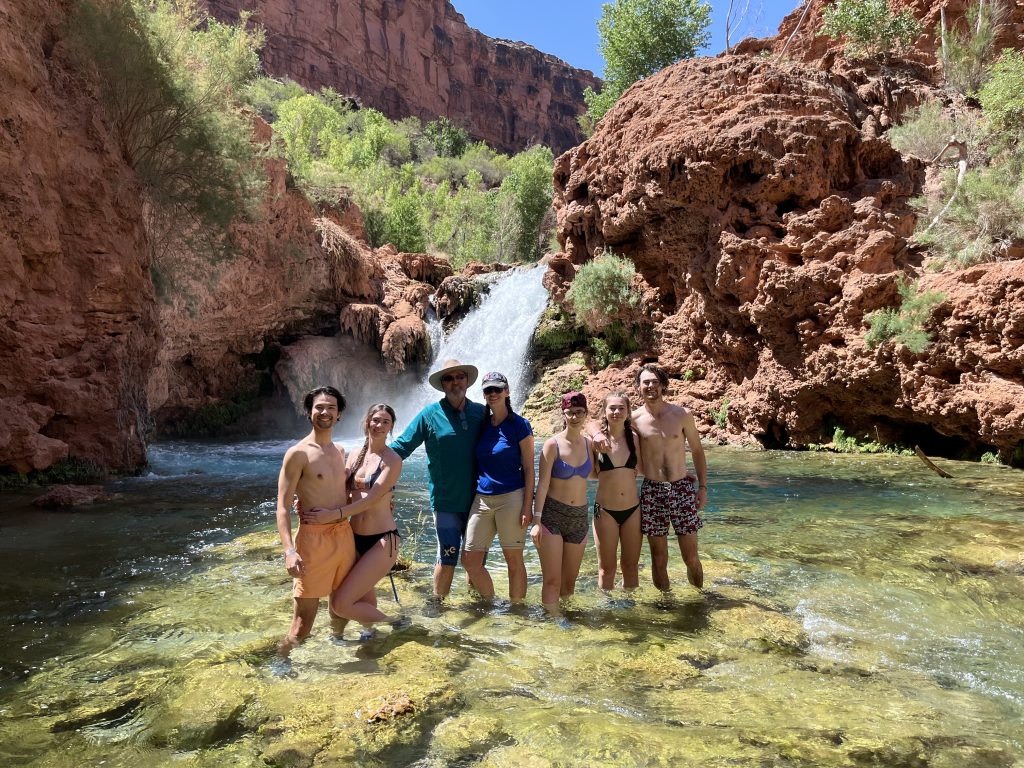 Daniel, Jaimie, Craig, Jen, Emma, Sarah, and Joshua standing in the water in front of Hidden Falls with canyon in the background.