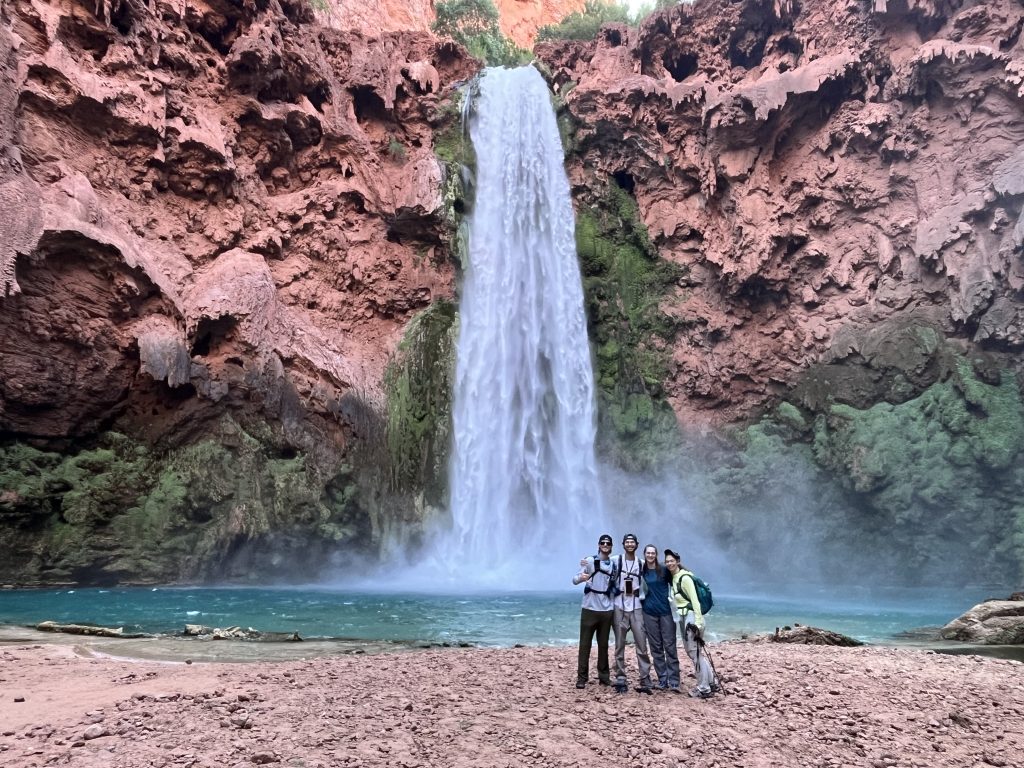 Joshua, Daniel, Jaimie, and Jen standing in front of Mooney Falls with the canyon walls and turquoise pool in the background