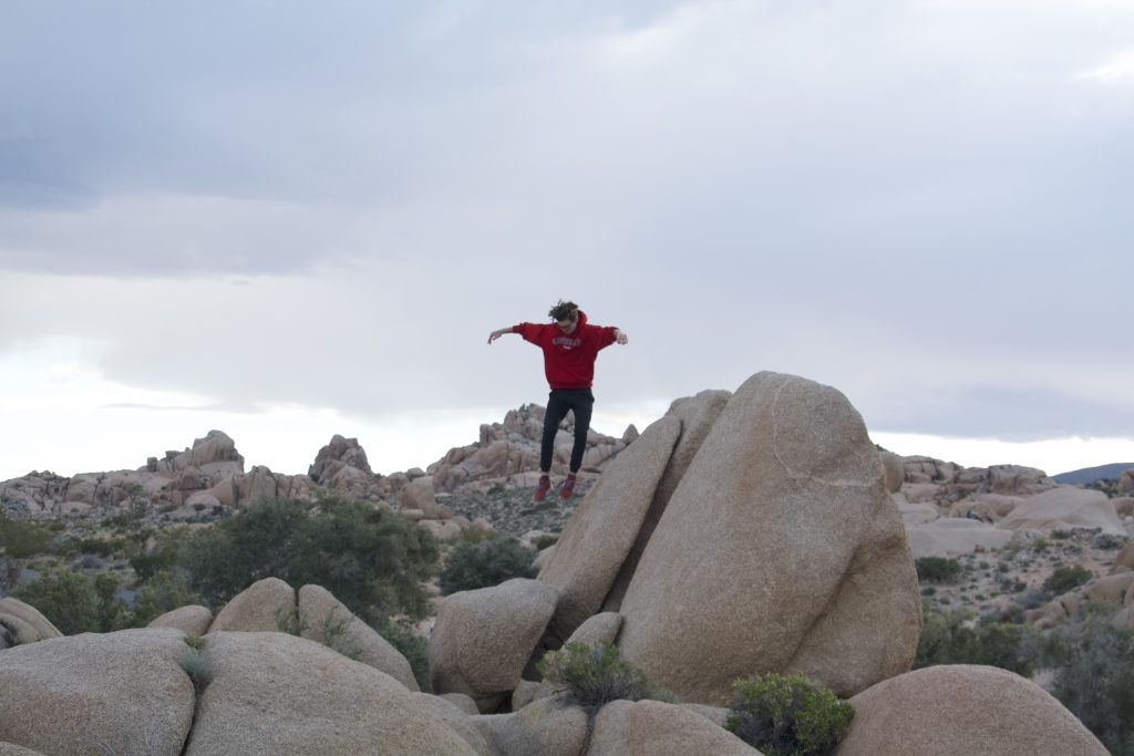 Joshua mid air jumping off one boulder to another boulder lower down near Jumbo Rocks Campground in Joshua Tree National Park