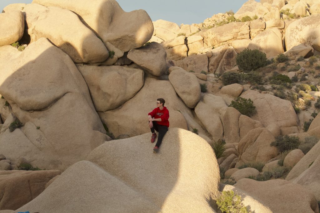 Joshua sitting on a massive boulder in the middle of the jumbo rock formations, looking out into the distance.