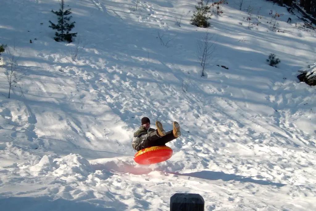 Person riding a bright red toboggan down a snowy hill in a Saskatoon neighbourhood park during winter.