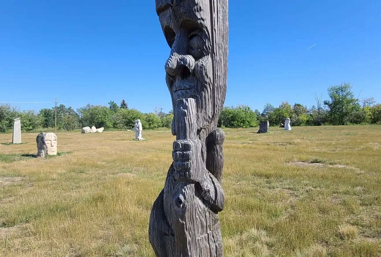 Carved wooden sculpture standing in an open grassy field at the University of Saskatchewan outdoor sculpture garden.
