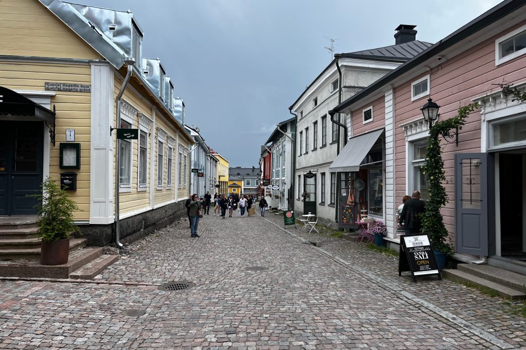 Cobblestone street in Old Porvoo. Colourful businesses along the street and tourists on the road.