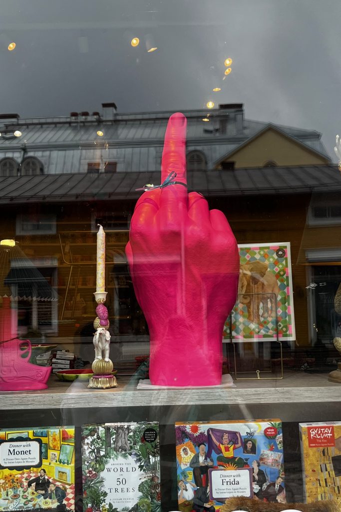Shop window with a sculpture of a fist holding up the middle finger with puzzles on a shelf below.
