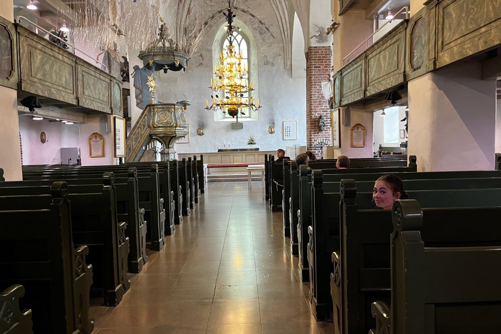 Inside Porvoo Cathedral, Sarah is sitting in one of many rows of pews.