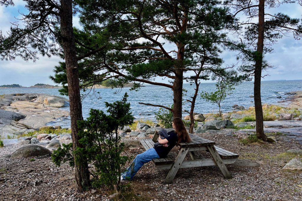 Sarah sitting at a picnic table looking out at the rocky shoreline along the Porkkalanniemi shoreline of the Baltic Sea.