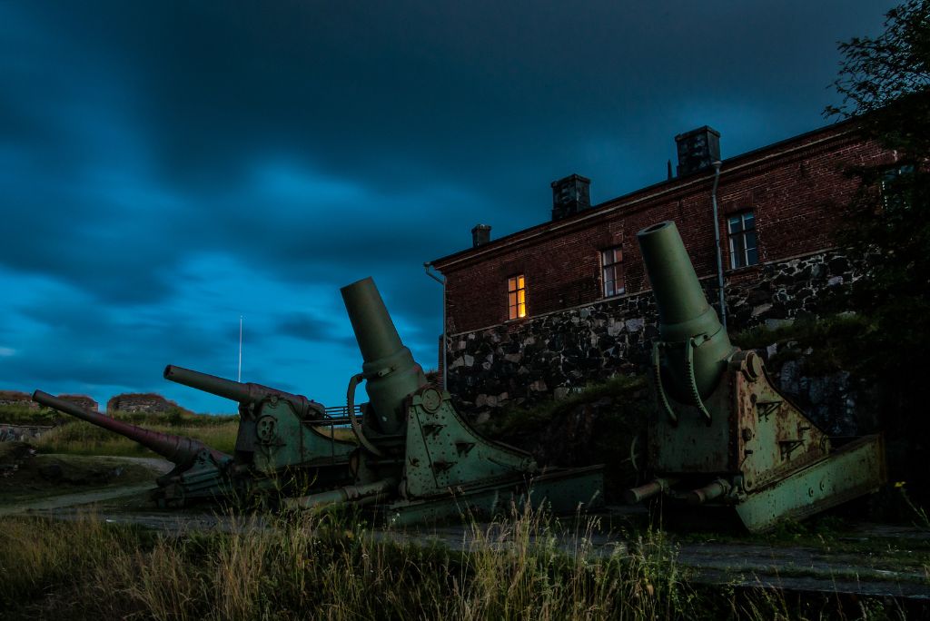 Cannons outside a historic building at Suomenlinna Fortress, Helsinki, with interior lights on, showcasing preserved guardhouse or museum