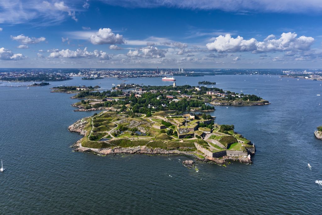 Aerial view of the Suomenlinna archipelago with Helsinki skyline and ferry in the background.