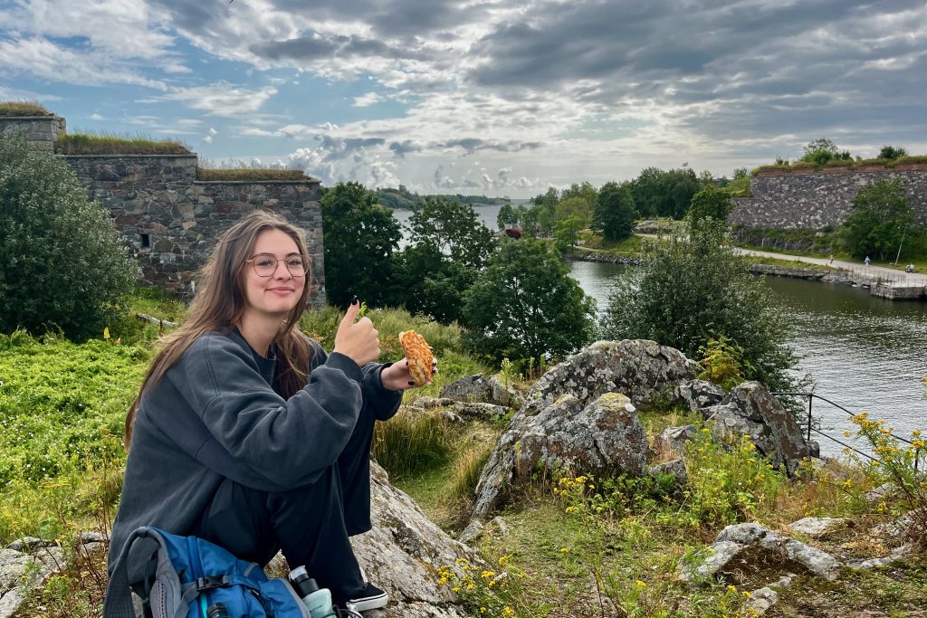 Woman eating a picnic lunch at a grassy spot near the channel with fortress wall in the background.