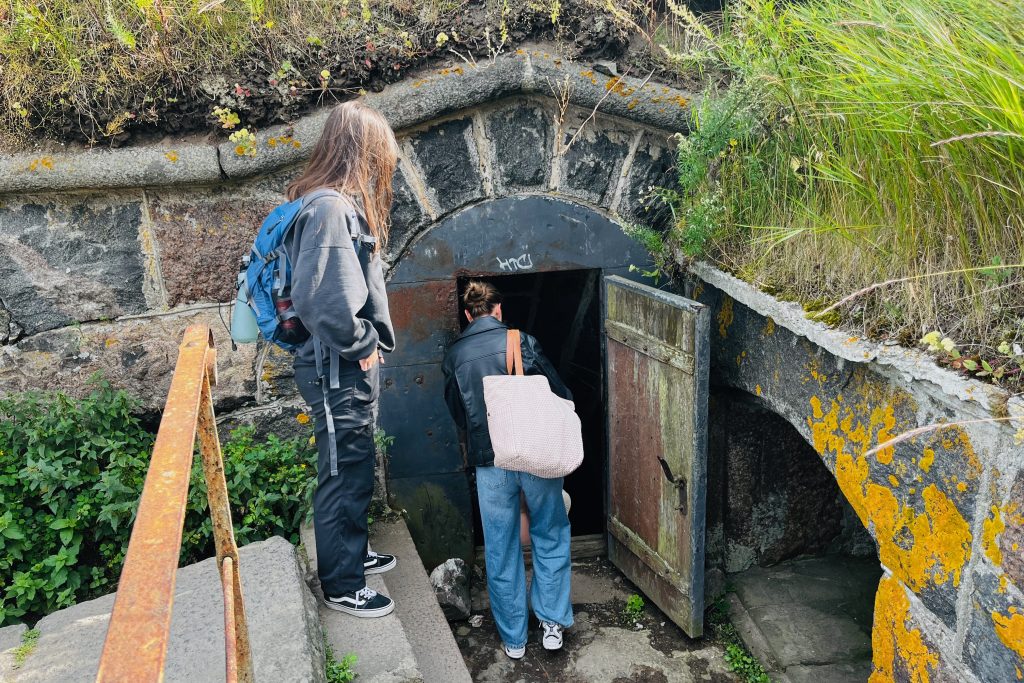 Two visitors standing at the entrance of a stone bunker in Suomenlinna, with one person peering inside the dark tunnel beneath the fortress walls.