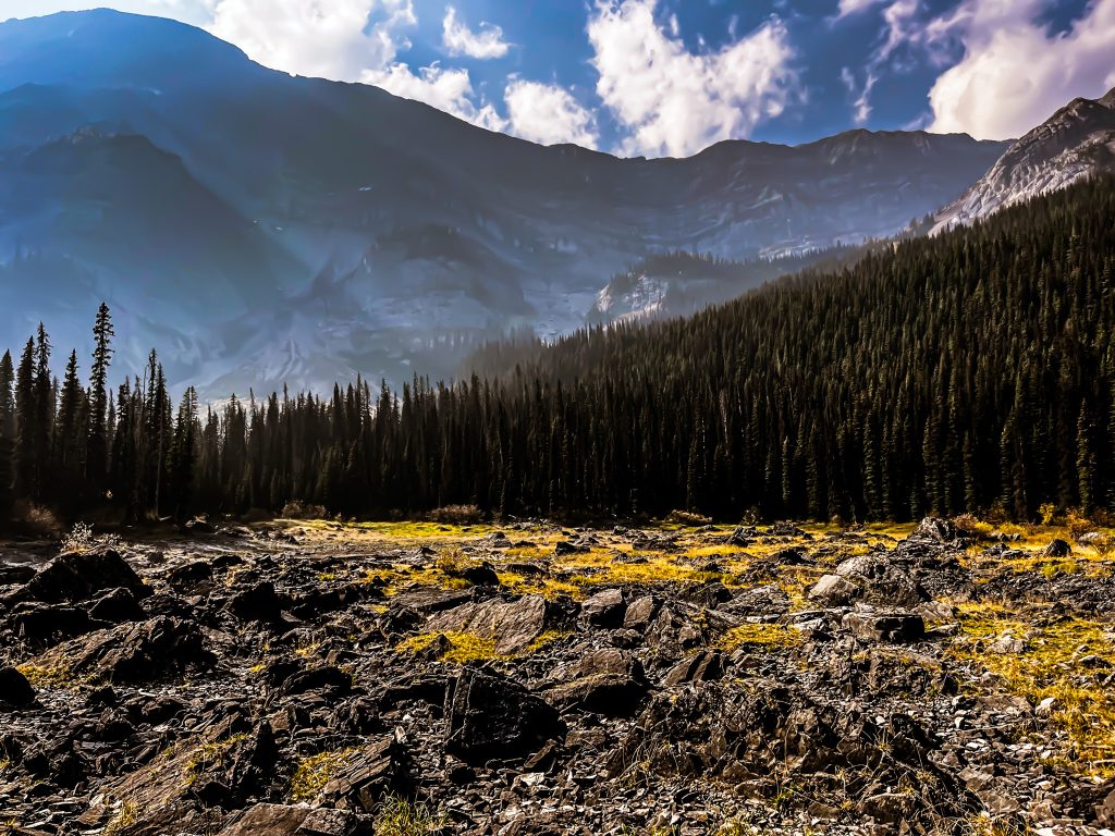 Off the beaten path Kananaskis hikes A dried up lake full of boulders where Warspite Lake used to be. Trees and mountains in the background.