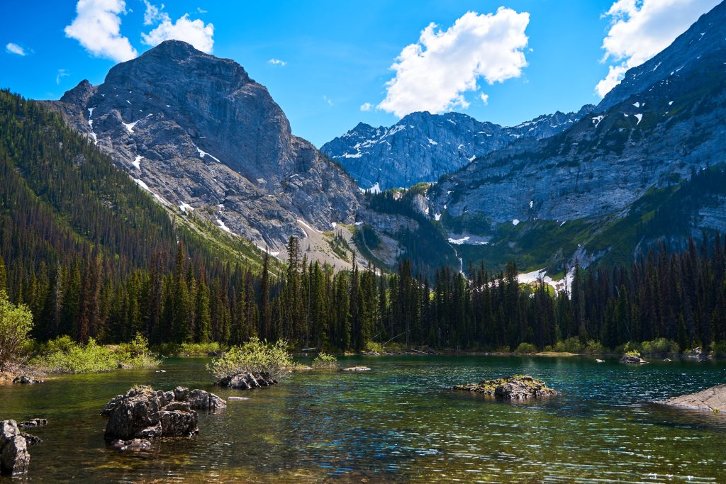Off the beaten Path Kananaskis hikes Warspite Lake with rocks in the mid ground and trees and mountains in the background.