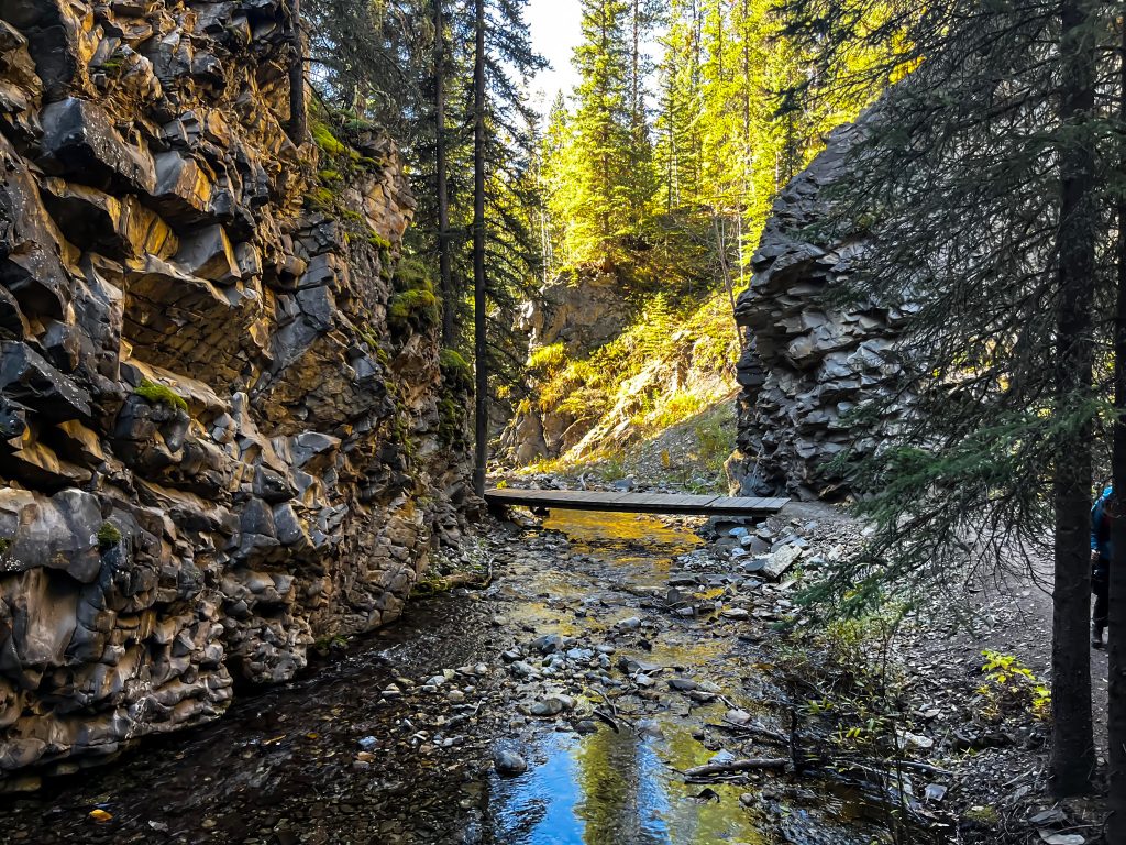 Off the beaten path Kananaskis hikes a river funning through a canyon with a bridge connecting the two sides. canyon walls on either side of the river.
