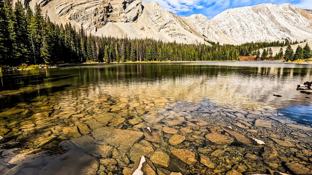 off the beaten path Kananaskis hikes First Picklejar Lake with rocks visible beneath the crystal clear water, mountains and trees reflecting in the lake, and mountains and trees in the background