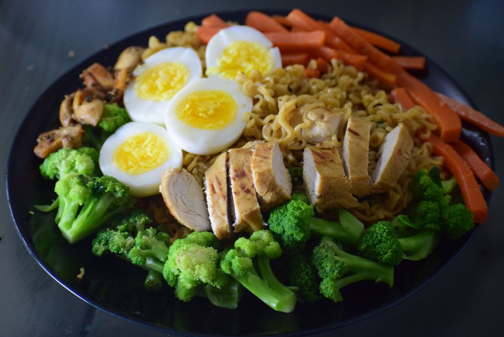 hiking fuel for high elevations A plate with a complete post hike meal, including hard boiled eggs, chicken, broccoli, ramen, carrots, and mushrooms.