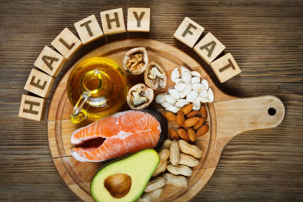 hiking fuel for high elevations cutting board with an array of healthy fats displayed, including avocado, salmon, peanut, almonds etc, with tile letters above spelling healthy fats