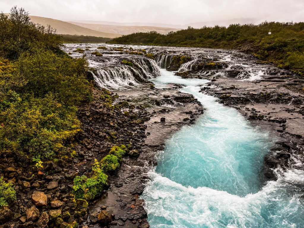 Brúarfoss waterfall with turquoise water and the river flowing downstream from the falls.