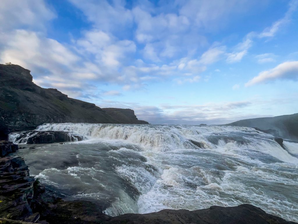 Close-up view of Gullfoss waterfall from a nearby observation point, showing only the top of the upper and lower tiers, with bright blue sky.