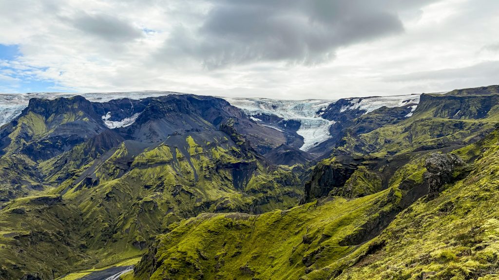Laugavegur and Fimmvörðuháls combo Landscape photo taken at the top of the initial Fimmvörðuháls ascent, featuring a broad valley and distant glacier-covered mountains.