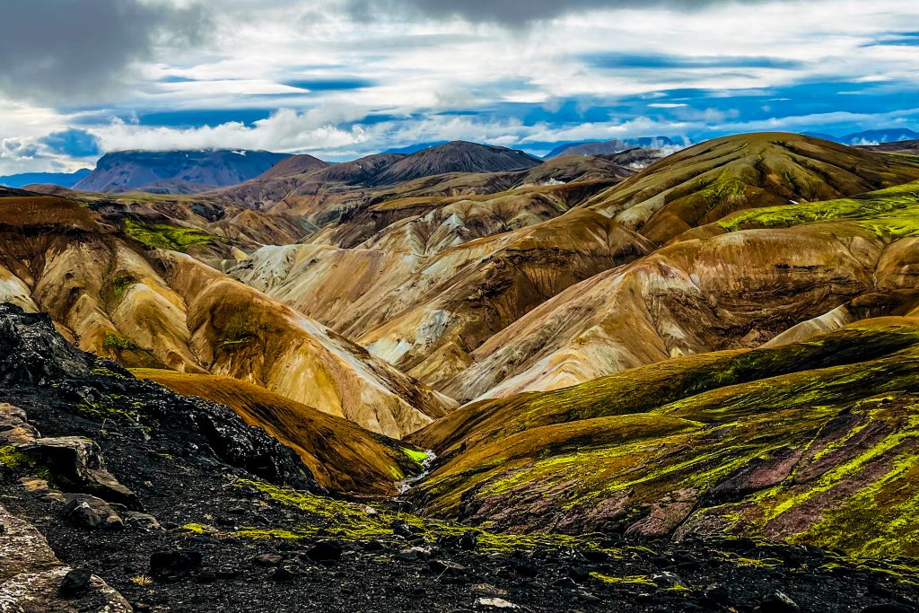 Laugavegur and Fimmvörðuháls combo Rhyolite mountains on the Laugavegur Trail with Black volcanic ash and rocks in the foreground and blue sky