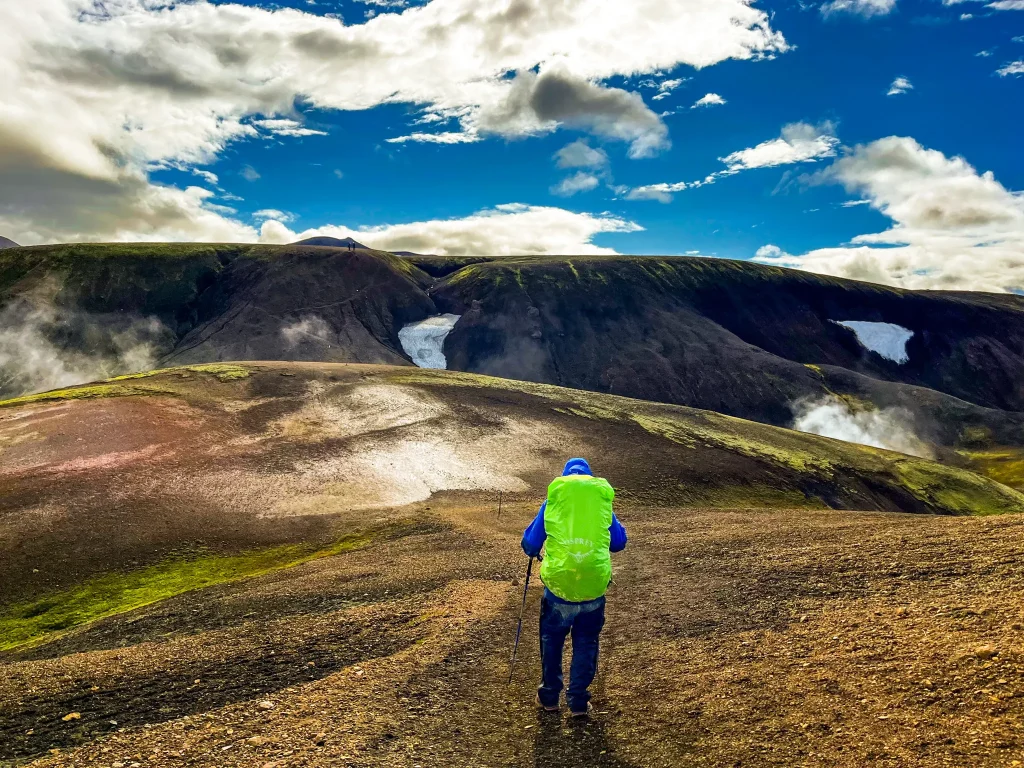 Hiker with a bright green pack descending a volcanic ridge between Landmannalaugar and Hrafntinnusker in Iceland’s highlands