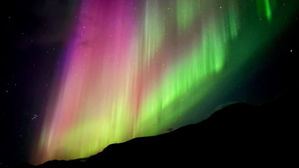 Laugavegur and Fimmvörðuháls combo bright green and pink northern lights against a black night sky at Álftavatn campground