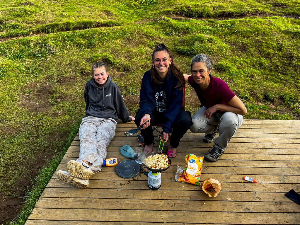 three hikers cooking lunch on a wooden boardwalk with grass in the background