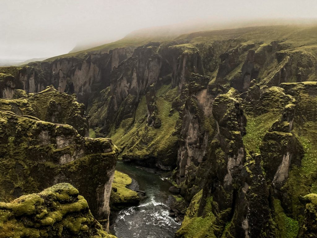 View into Fjaðrárgljúfur canyon with steep, moss-covered basalt cliffs and the Fjaðrá River winding through the narrow gorge below.
