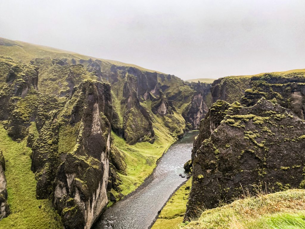 River winding between mossy green cliffs with foggy grey sky above