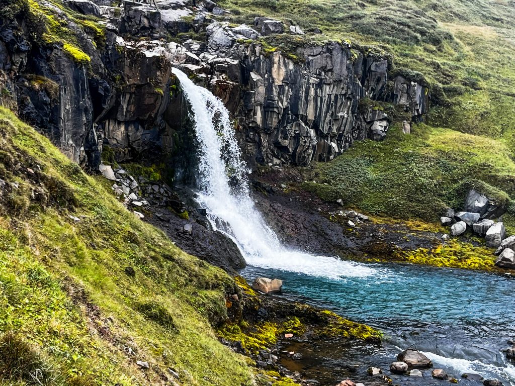 Waterfall plunging into crystal clear, blue water below with basalt columns on either side