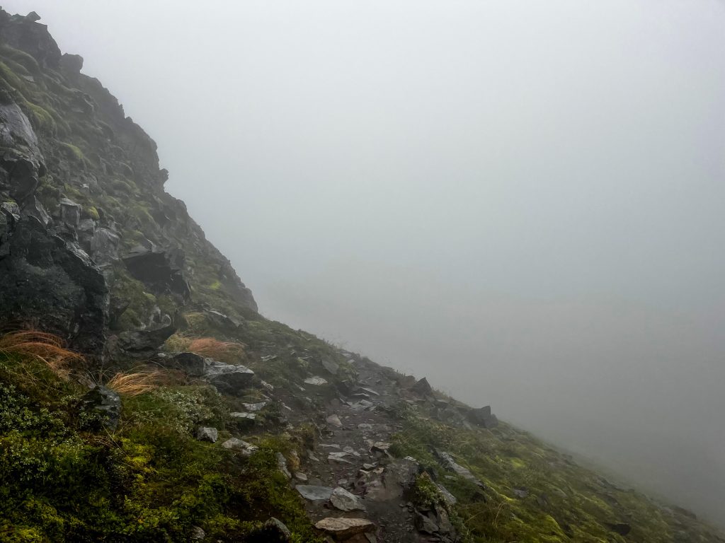 Rocky cliffside trail with whitout fog conditions ahead that obscure the trail.