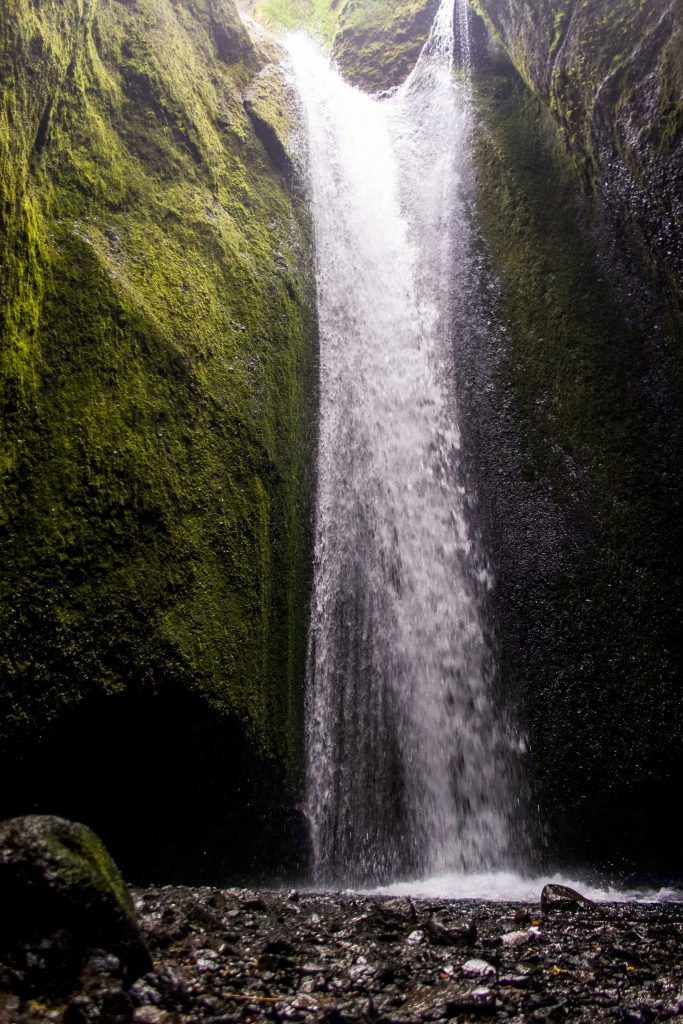 Waterfall at the end of Nauthúsagil Ravine, framed by steep canyon walls and rugged terrain.