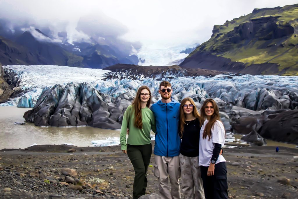 Hikers posing in fronof the deeply crevassed glacier with mountains on either side and a foggy frey sky above