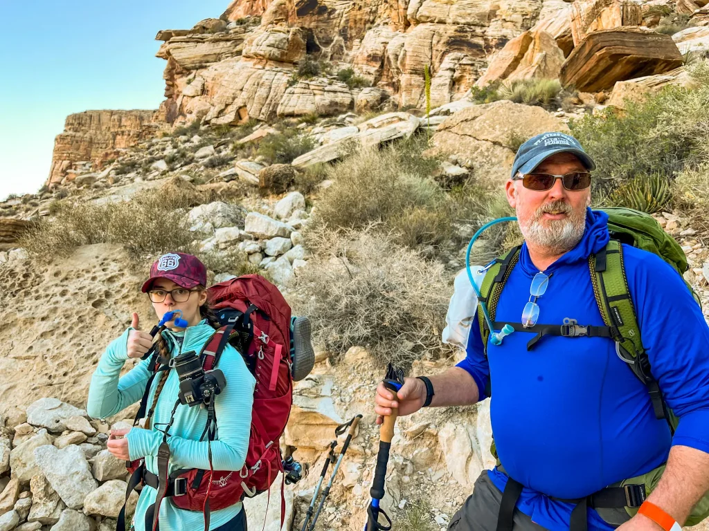 Two hikers on the Havasupai trial stopping for a water break. Canyon rock walls behind htem