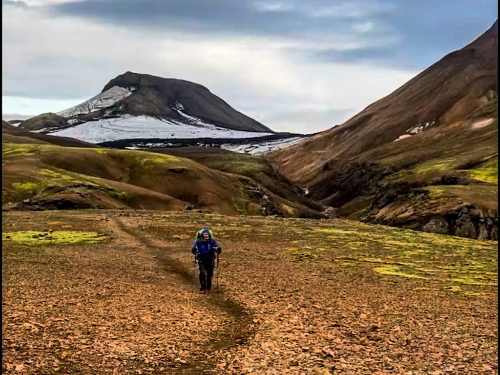 Backpacker hiking across volcanic terrain near Hrafntinnusker with snow-covered peaks in the Icelandic highlands