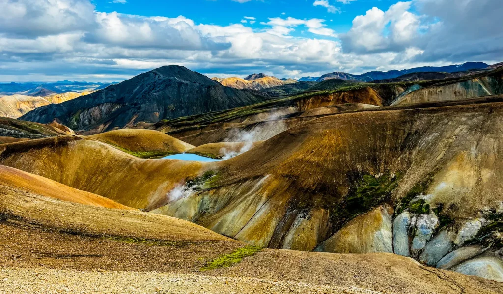 Colorful rhyolite mountains and steaming geothermal vents between Landmannalaugar and Hrafntinnusker in Iceland’s highlands under a partly cloudy sky