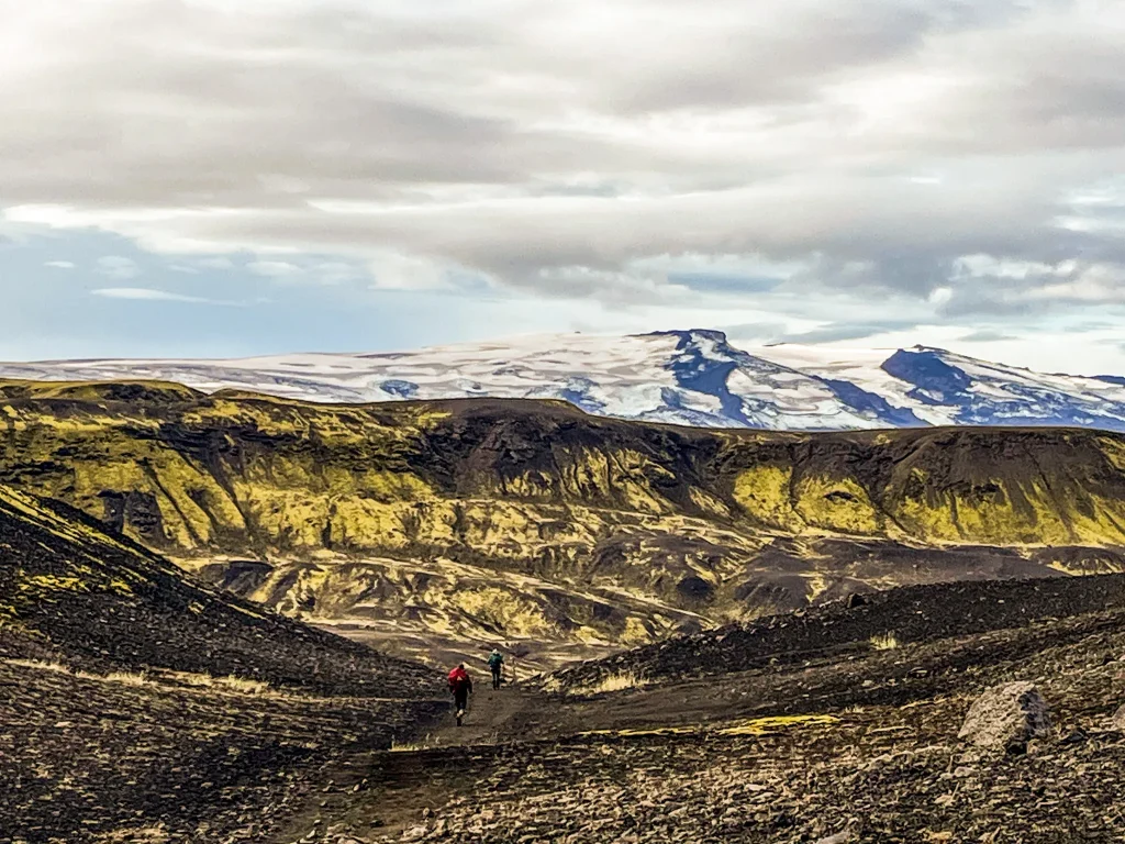 Hikers crossing exposed volcanic terrain between Álftavatn and Emstrur with glacier-covered peaks in the distance
