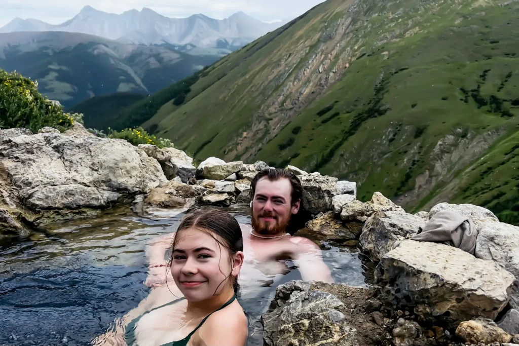 Two people relaxing in Mist Mountain hot spring overlooking the mountains in Kananaskis